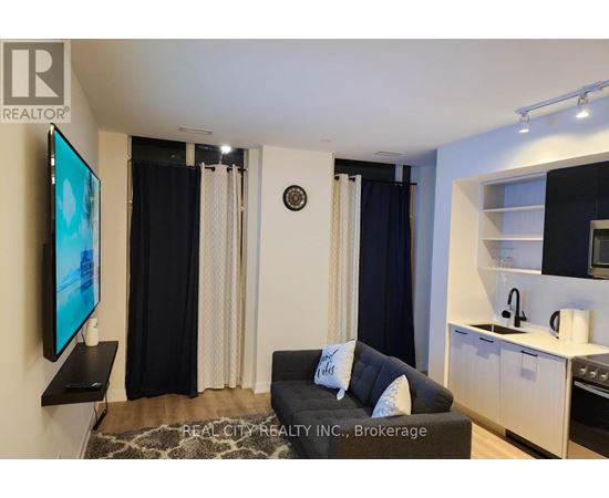 A living room with a couch, television, and kitchen area.