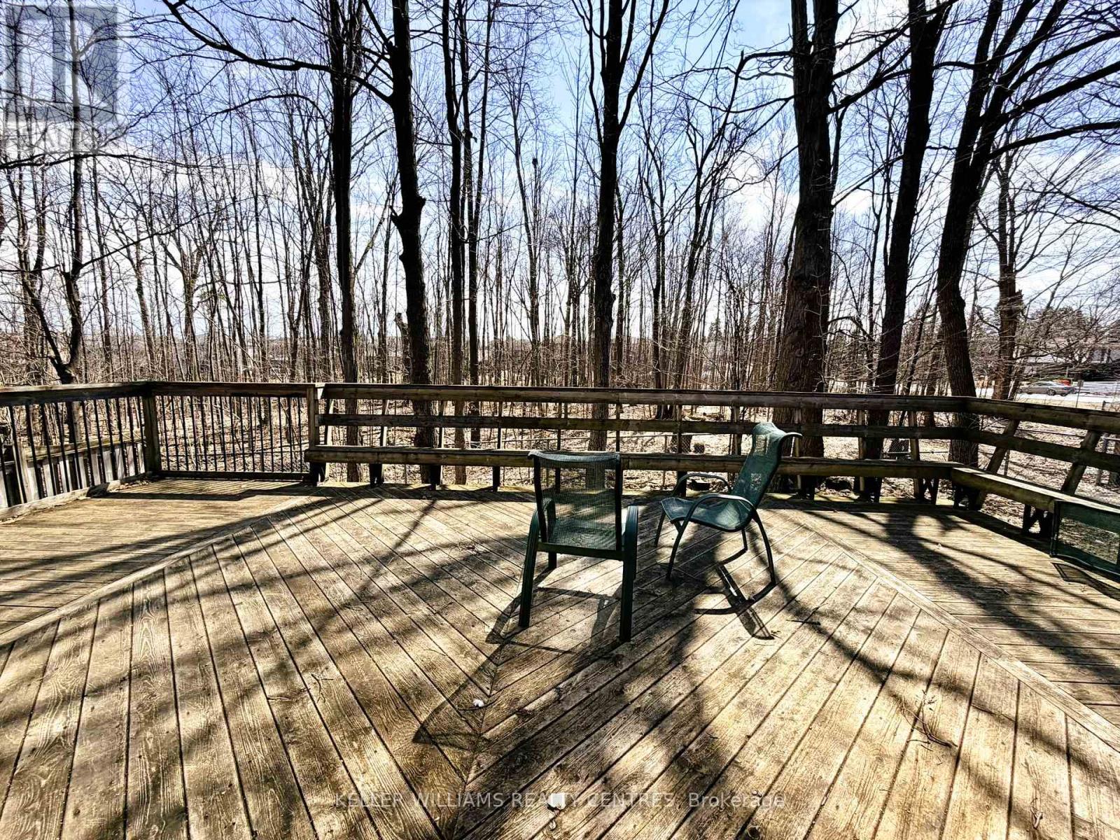 A wooden deck with a bench and trees in the background.