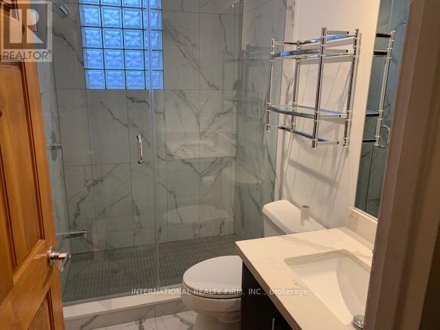A bathroom with a glass shower stall, toilet, and sink.
