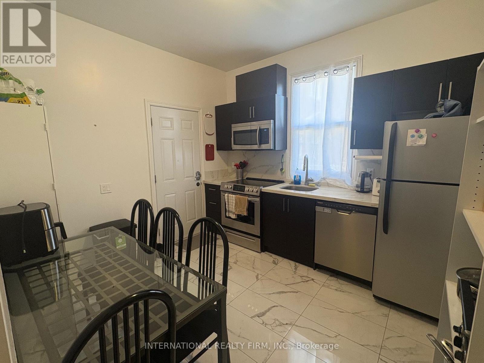 A kitchen with a table and chairs in the foreground and a refrigerator, microwave, and oven in the background.