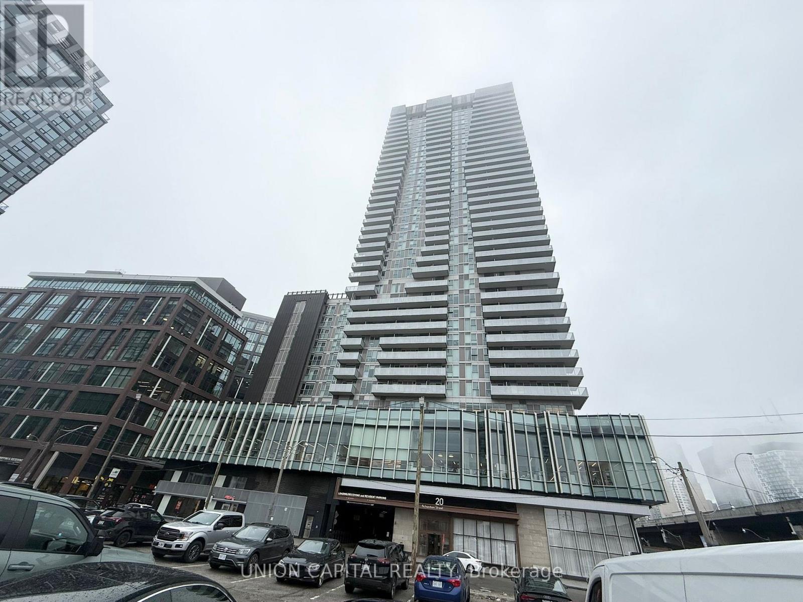 A tall building with a glass facade stands in the foreground of a city street.