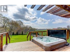 A hot tub is on a wooden deck with a view of a grassy field.