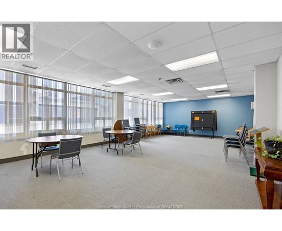 A conference room with a large table and chairs, a television, and a plant on a desk.