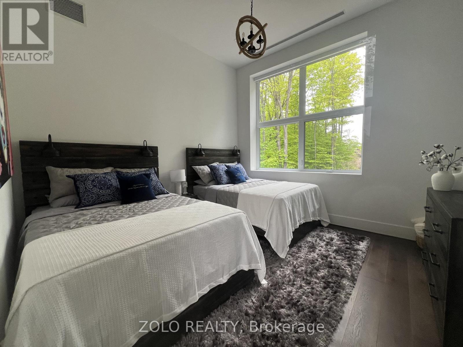 A bedroom with two beds and a window showing trees outside.