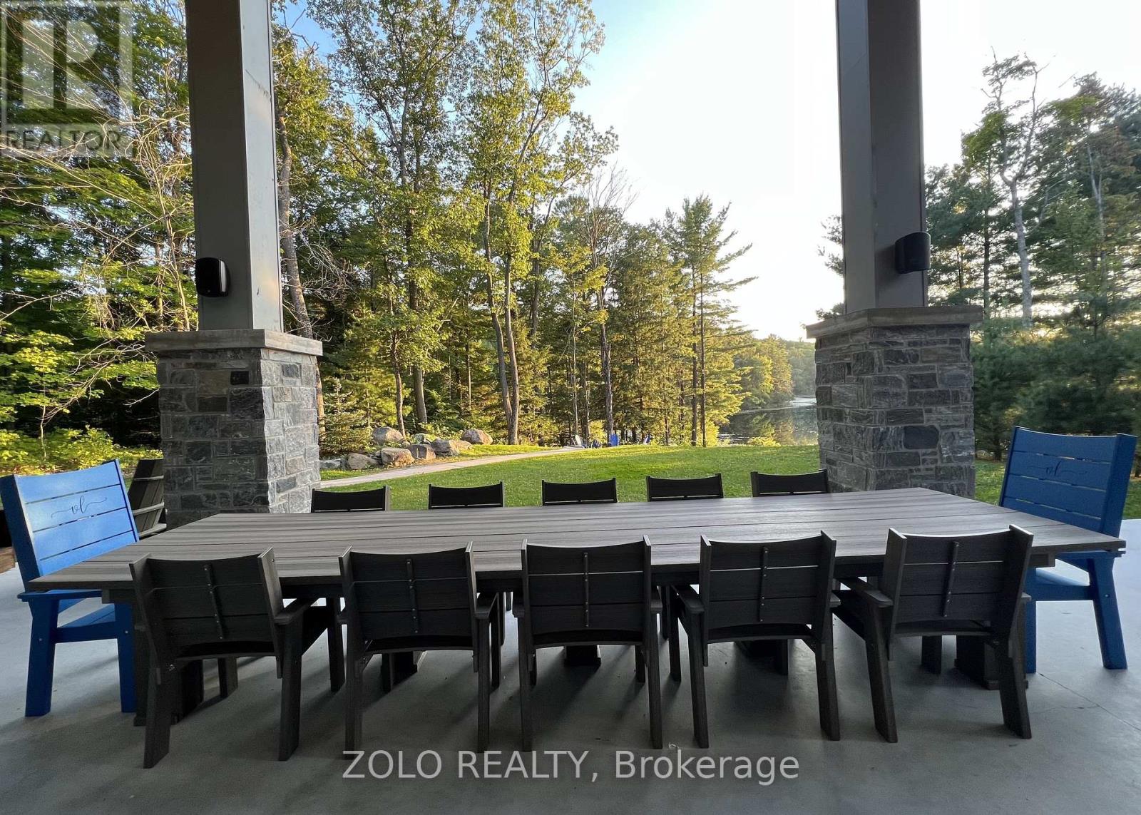 A table set for six with chairs in front of a stone pillar and trees in the background.