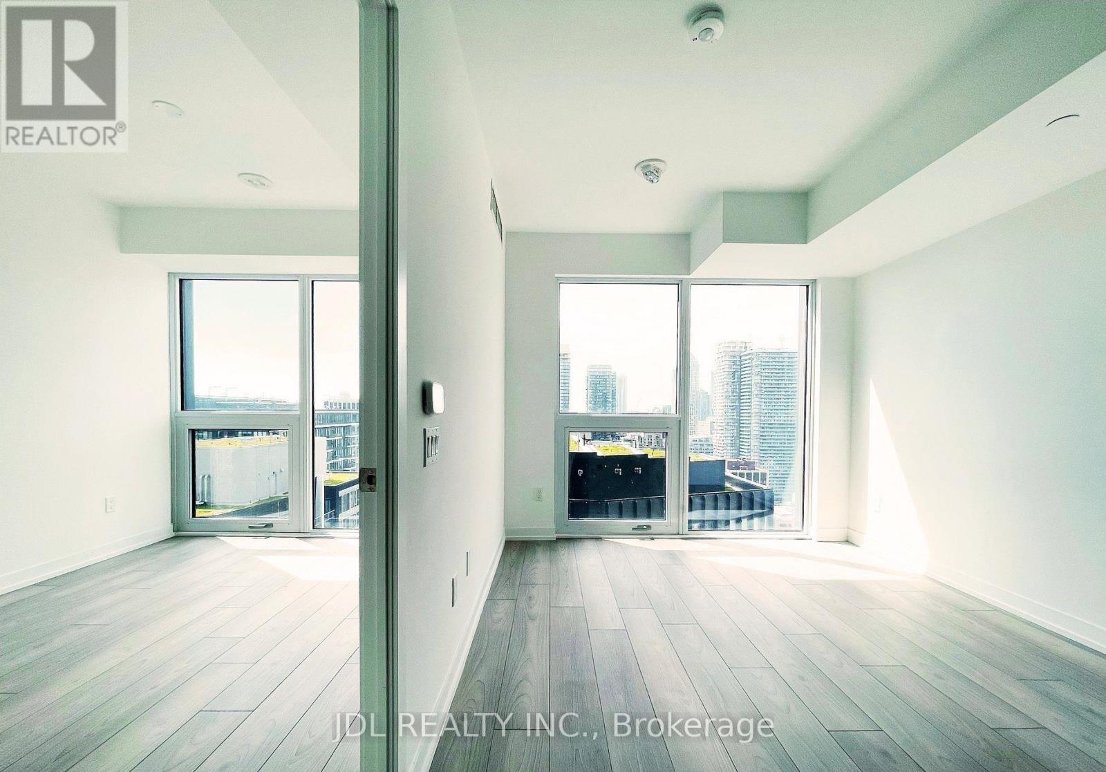 A spacious room with wooden floors and large windows overlooking a cityscape.