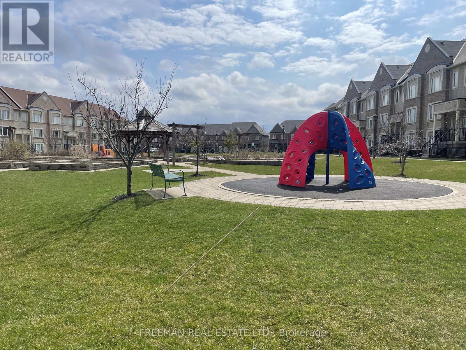 A playground with a red and blue slide in the middle of a grassy area.