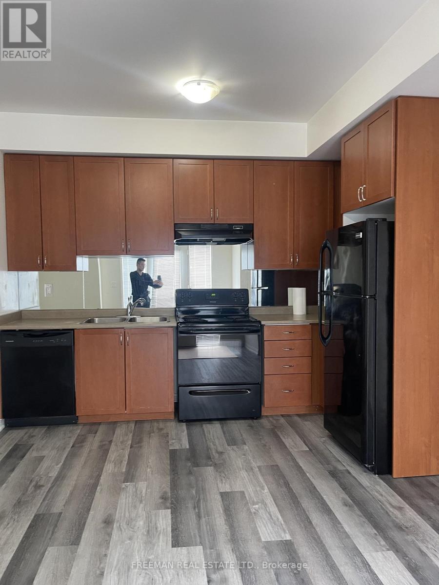 A man is standing in a kitchen with wooden cabinets and black appliances.