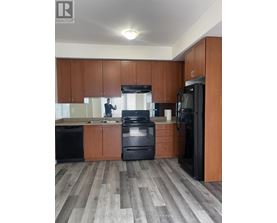 A man is standing in a kitchen with wooden cabinets and black appliances.