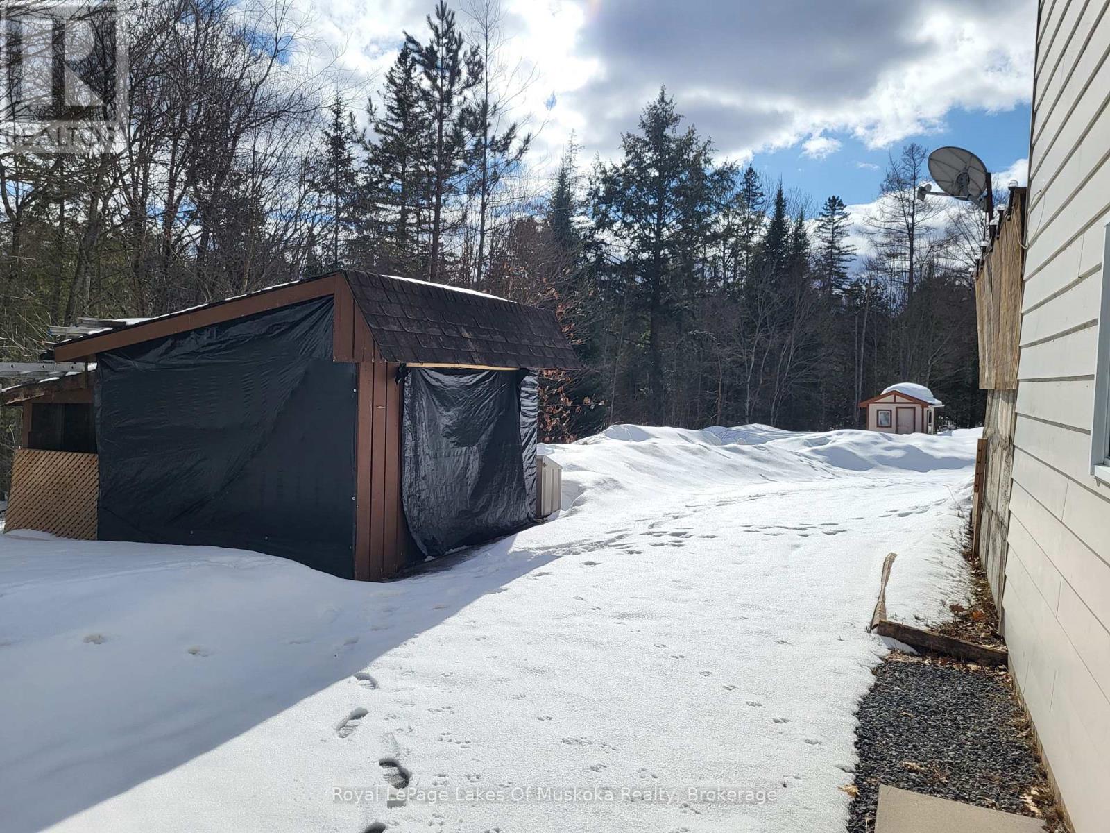 A shed covered in a black tarp sits in a snowy backyard.