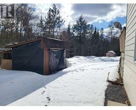 A shed covered in a black tarp sits in a snowy backyard.