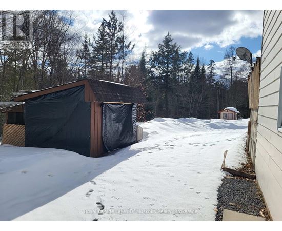 A shed covered in a black tarp sits in a snowy backyard.