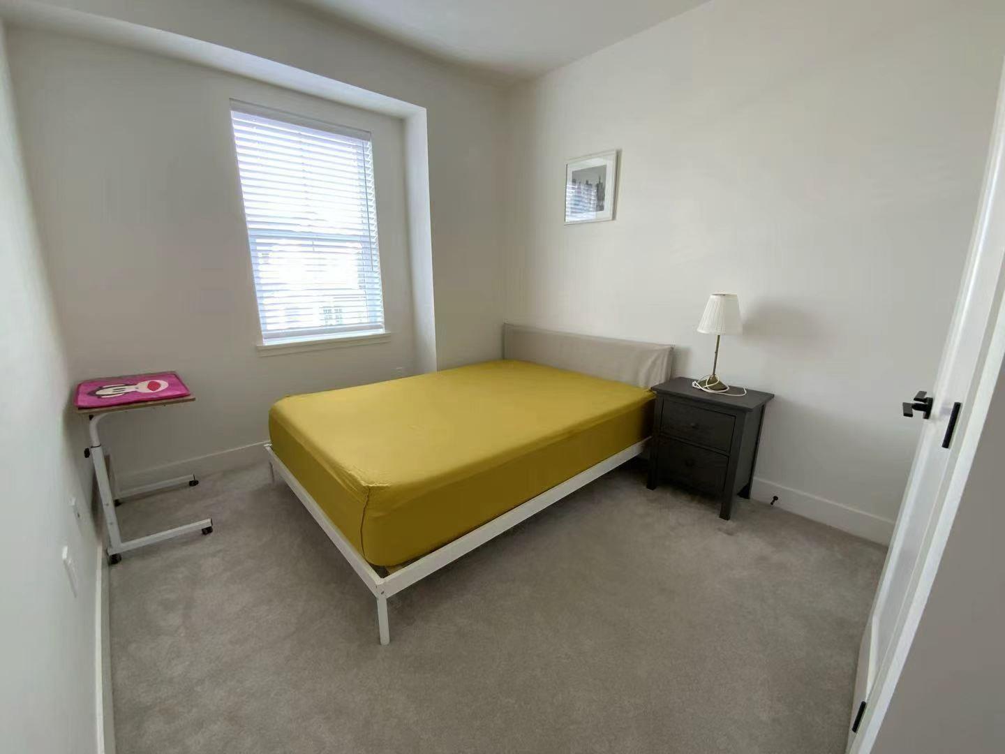 A bedroom with a bed, nightstand, and window.