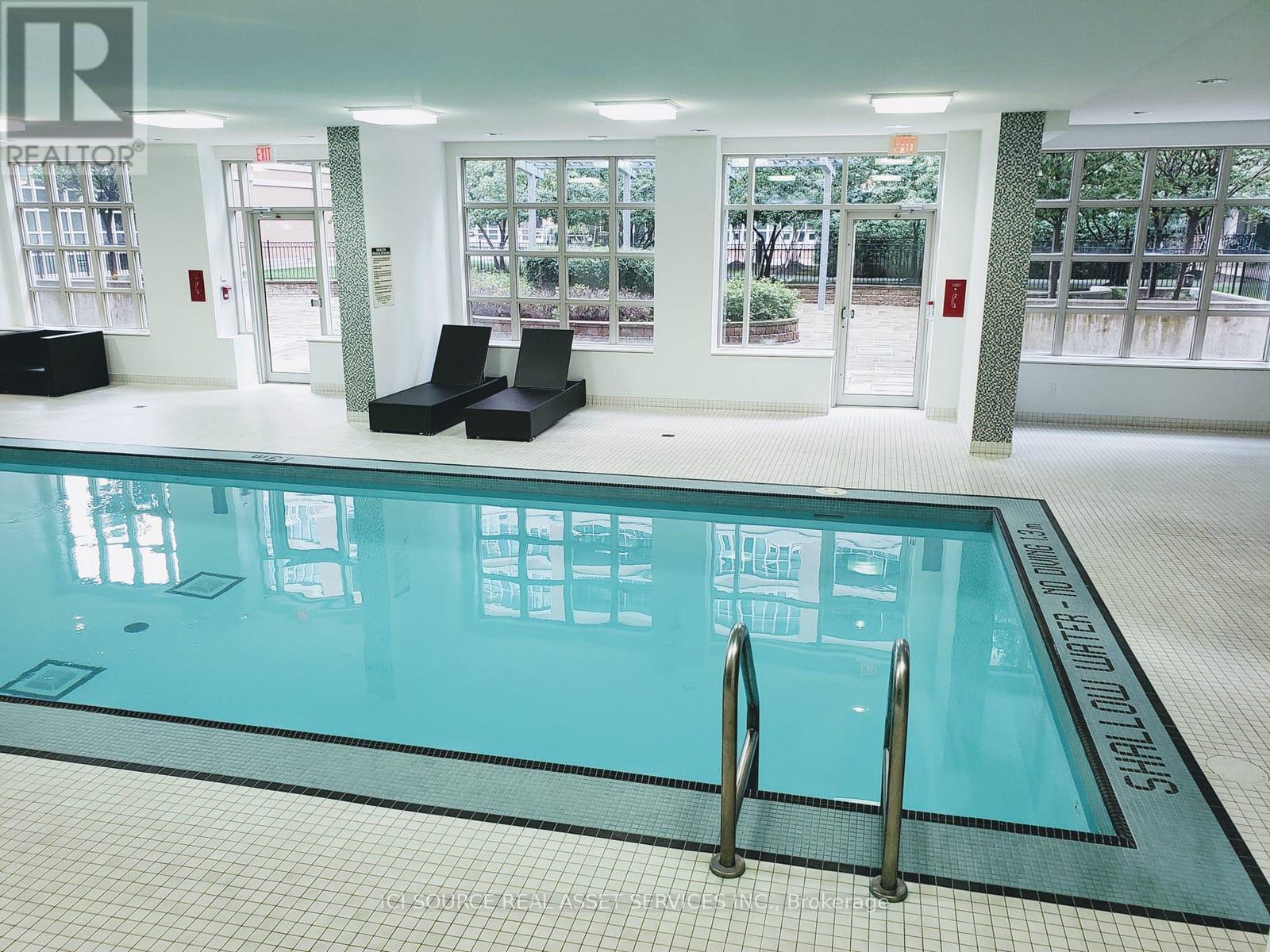 A large indoor swimming pool with a blue tiled edge and a black ladder.
