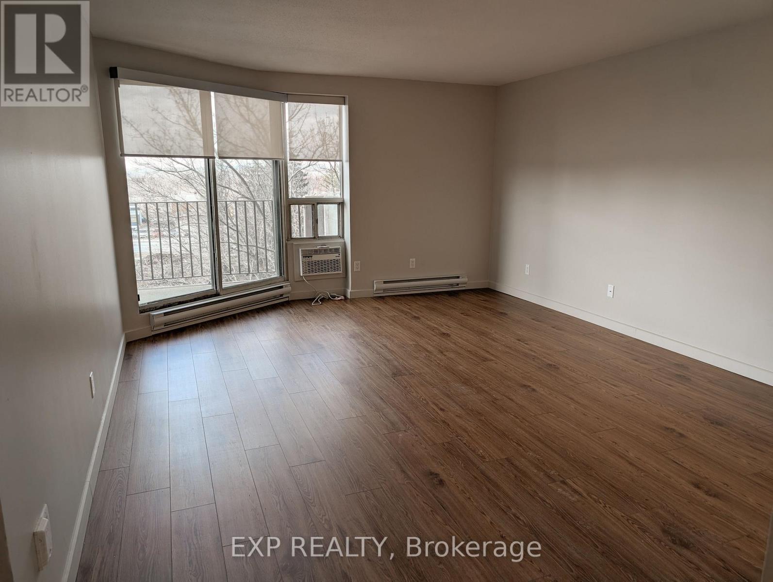 A room with wooden flooring and a large window with a view of a fence and trees.