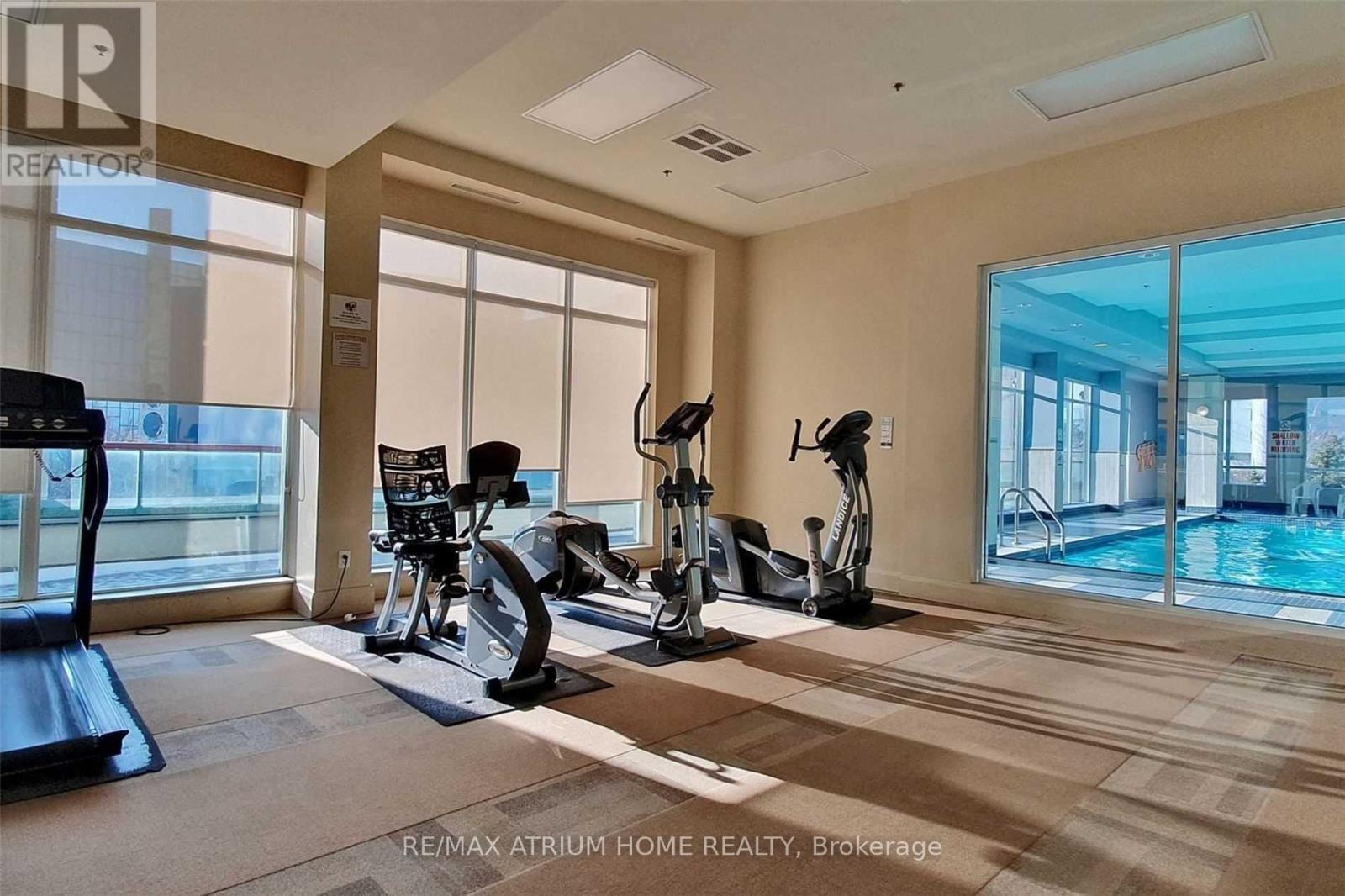 A well-lit gym with treadmills, exercise bikes, and a view of the pool outside.