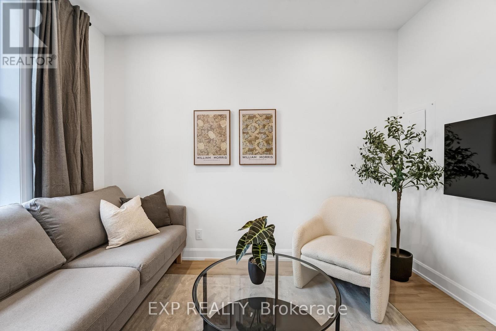 A living room with a grey couch, a white armchair, and a small tree on a glass table.