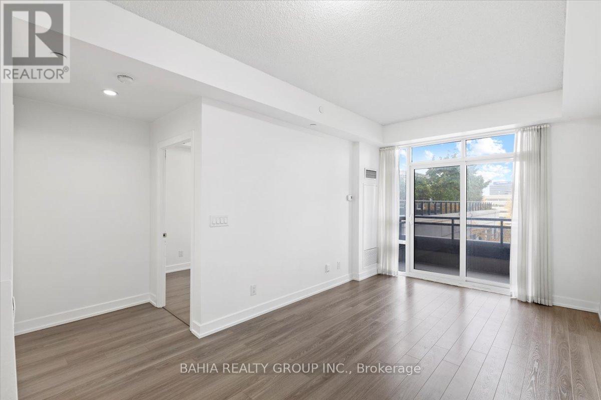 A spacious room with wooden flooring and white walls, with a sliding glass door leading to a balcony.