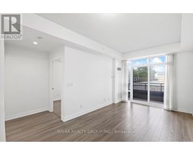 A spacious room with wooden flooring and white walls, with a sliding glass door leading to a balcony.