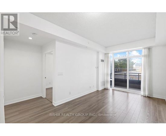 A spacious room with wooden flooring and white walls, with a sliding glass door leading to a balcony.