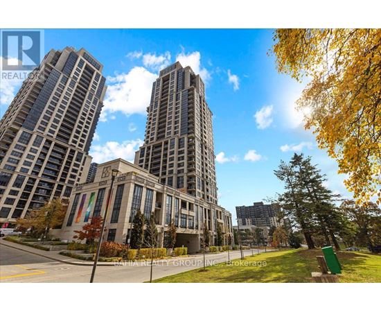 Two tall buildings are in the background of a tree with green leaves.