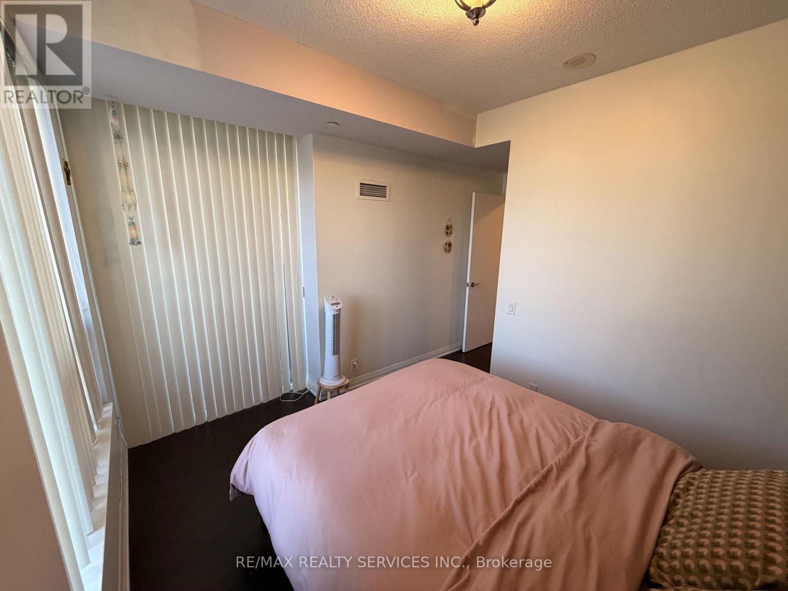 A bedroom with a bed covered in a pink sheet and a small closet with a door.