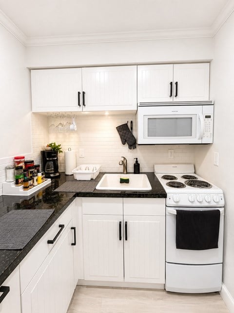 A white kitchen with black countertops and appliances.