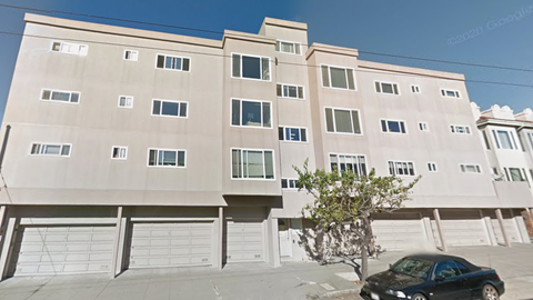 A black car is parked in front of a tan building.