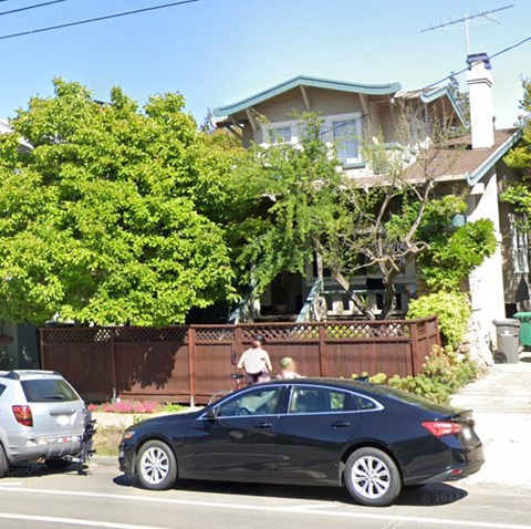 A black car is parked on the side of a street in front of a house.