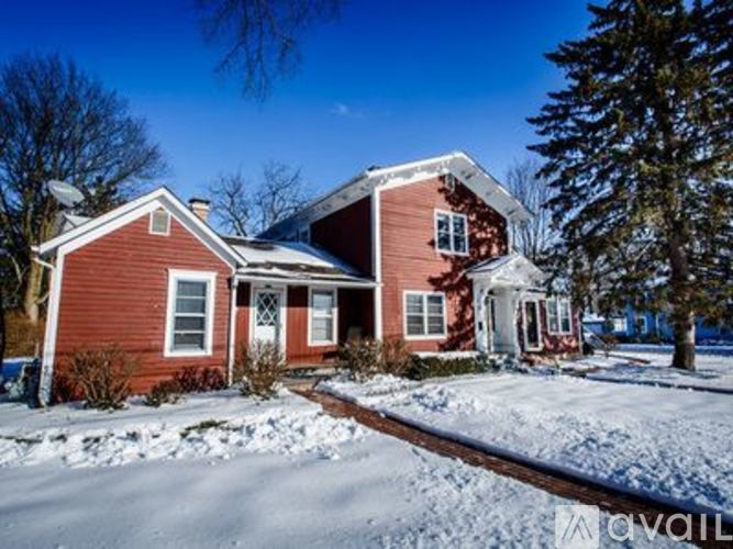 A red house with snow on the ground and trees in the background.