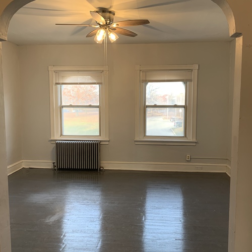 A room with a ceiling fan and two windows.