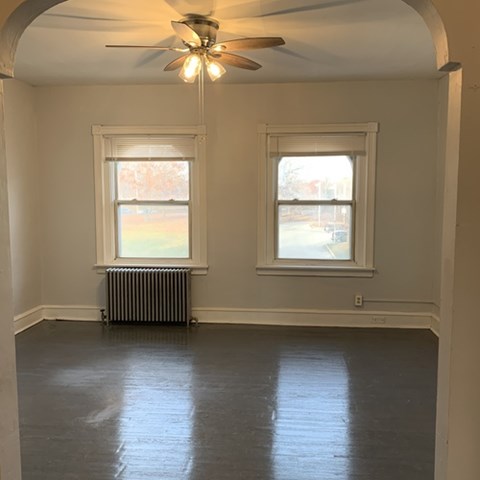 A room with a ceiling fan and two windows.