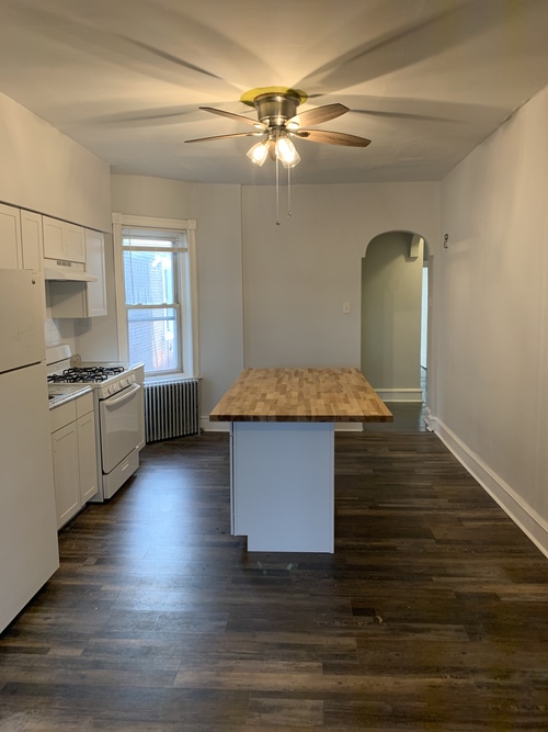 A kitchen with a white refrigerator, stove, and cabinets with a wooden island in the middle.