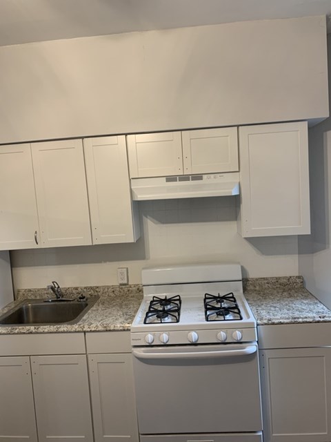 A white stove is in a kitchen with white cabinets.