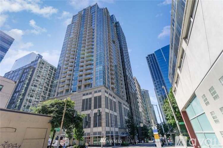 A tall building with many windows stands in the middle of a city street.