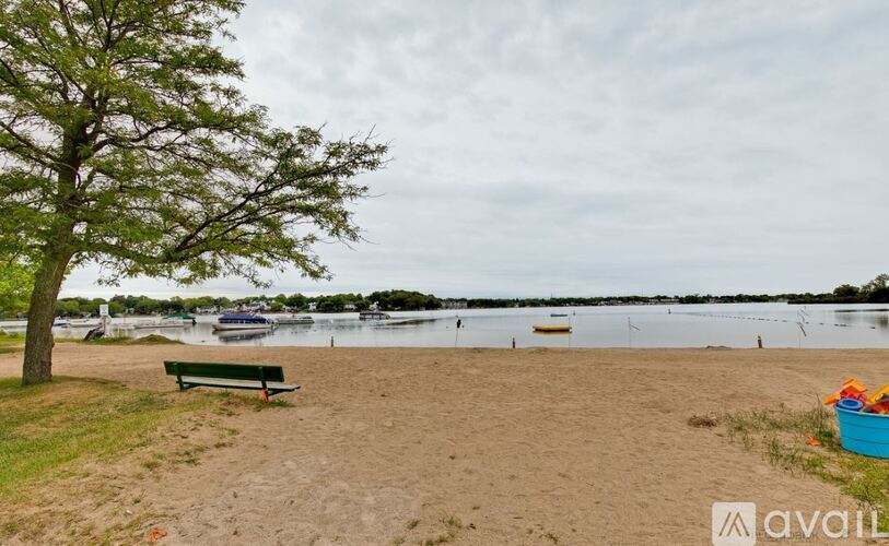 A beach scene with a bench, a tree, and boats in the water.