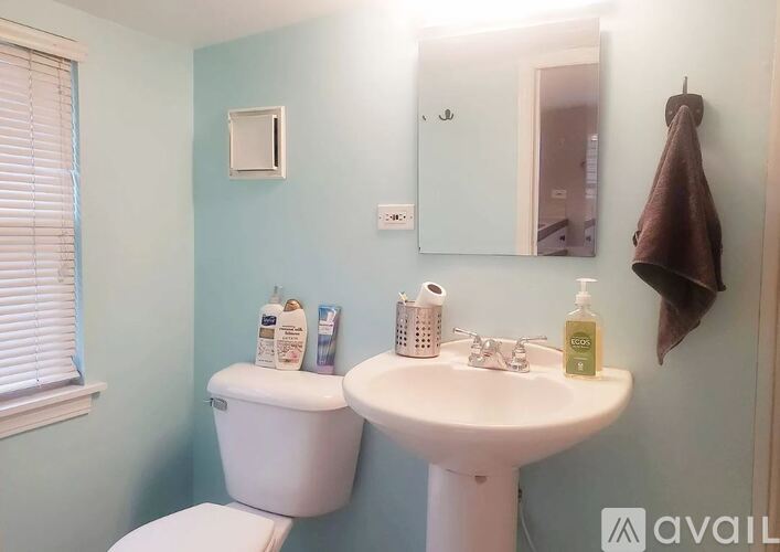 A bathroom with a toilet, sink, mirror, and towel rack.