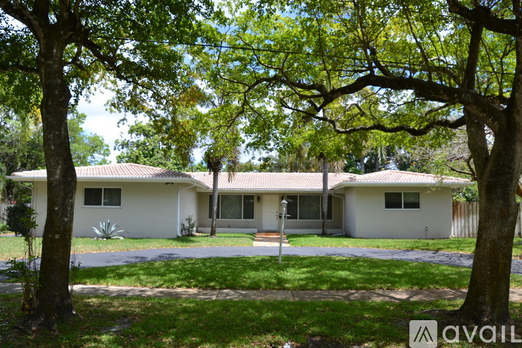 A house with a white exterior is surrounded by trees and has a driveway leading to the front door.