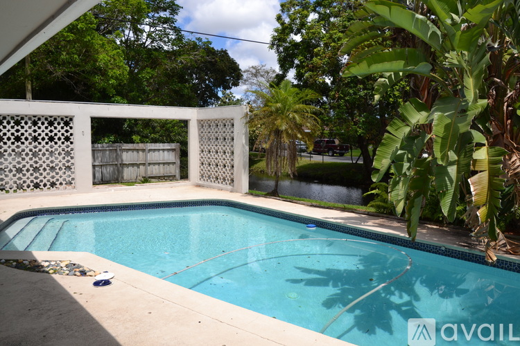 A pool surrounded by a white fence and green plants.