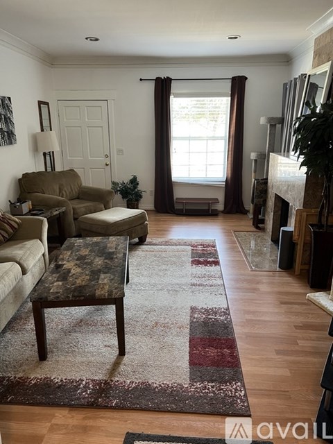 A living room with a rug, a couch, a chair, a table and a fireplace.