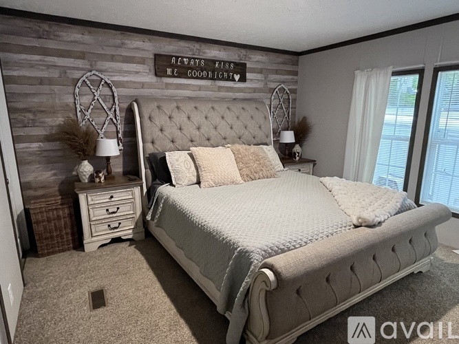 A bedroom with a large bed, a wooden headboard, and a wall decoration that says "AWAKENS KISSES WC GOODCHILD".