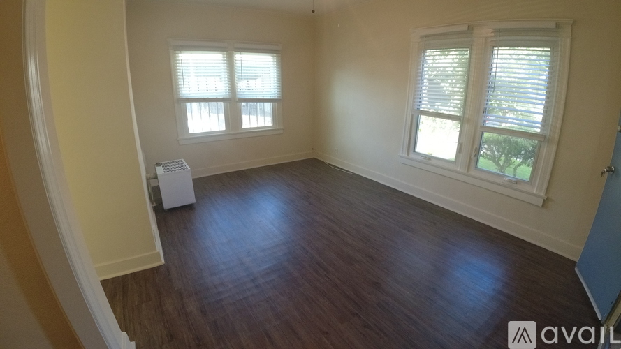 A room with wooden flooring and two windows.