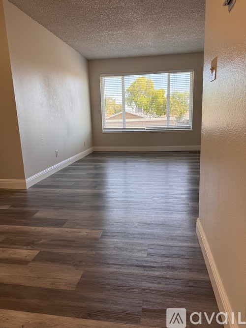 A room with wooden flooring and a window showing a view of trees.