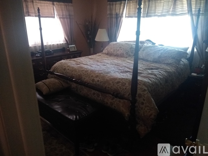 A bed with a floral patterned bedspread is in a room with a window and a lamp.