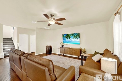 A living room with a brown leather couch and a ceiling fan.