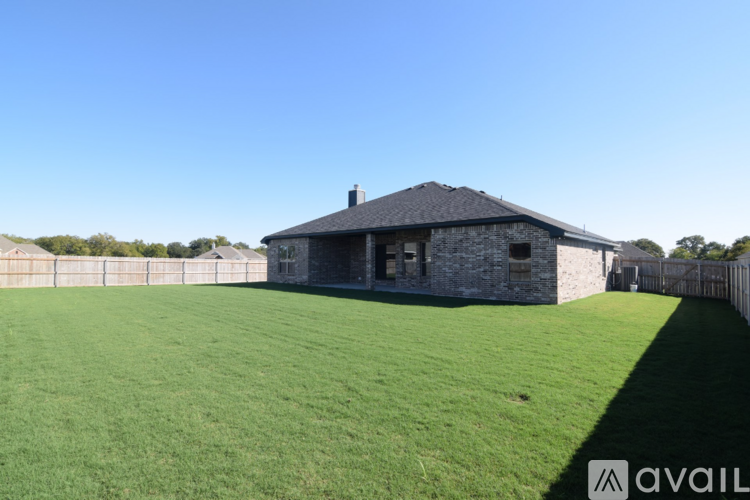 A house with a stone exterior and a black roof is surrounded by a green lawn and a fence.