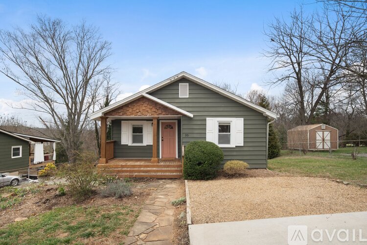 A house with a porch and a brown door is surrounded by trees and grass.