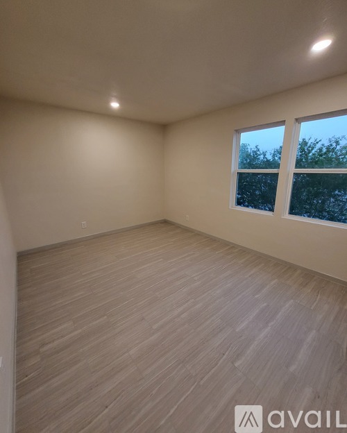 A room with wooden flooring and a window showing trees outside.