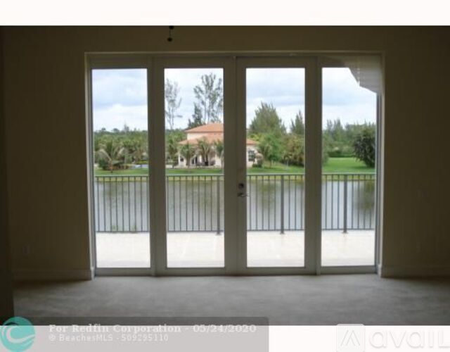 A room with a view of a fenced area and a building in the distance.