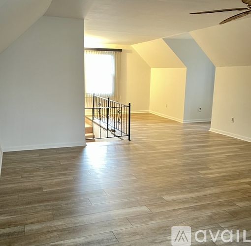 A spacious room with wooden flooring and a staircase with a metal railing.